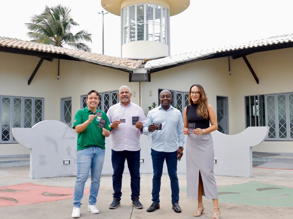 Quatro pessoas em pé, seguram o cartão Mais Aracaju Turista em frente ao Mirante da 13 de Julho