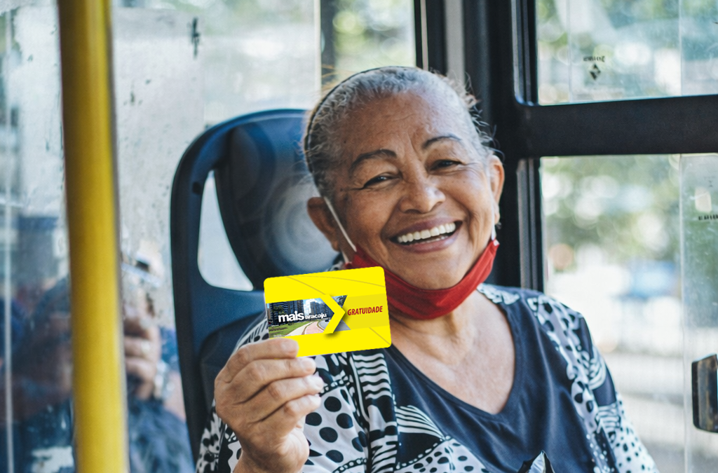 Idosa sorridente segura cartãos Mais Aracaju gratuidade no interior do ônibus