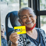 Idosa sorridente segura cartãos Mais Aracaju gratuidade no interior do ônibus