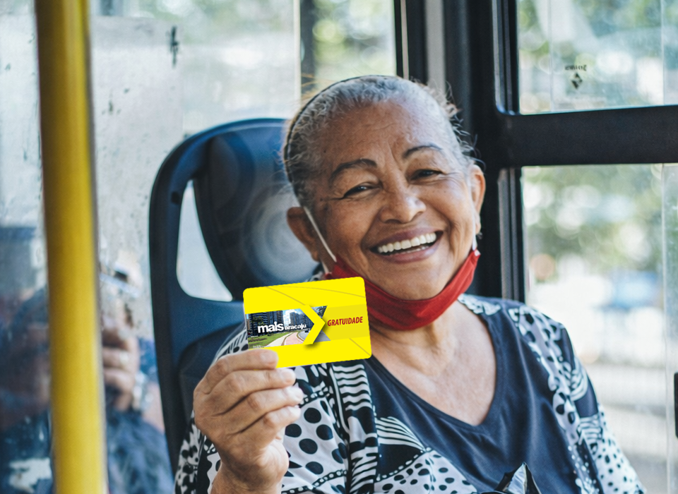 Idosa sorridente segura cartãos Mais Aracaju gratuidade no interior do ônibus