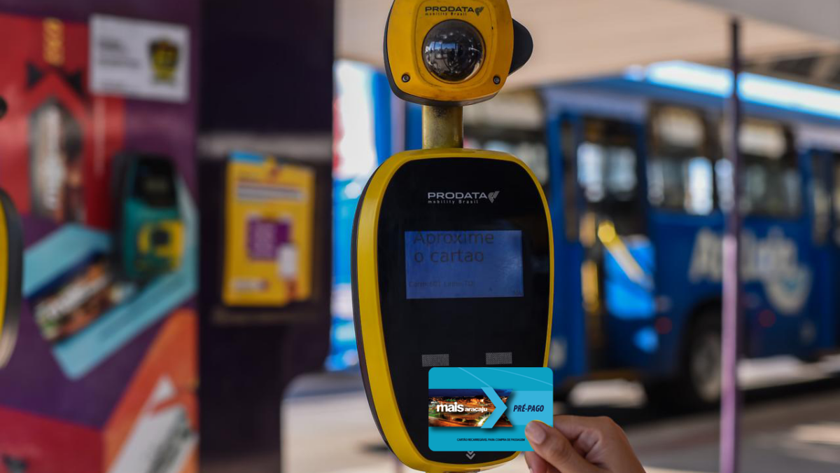 Mão feminina segura cartãos Mais Aracaju Pré-pago próximo a validador de bilhetagem em um terminal de ônibus