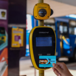Mão feminina segura cartãos Mais Aracaju Pré-pago próximo a validador de bilhetagem em um terminal de ônibus